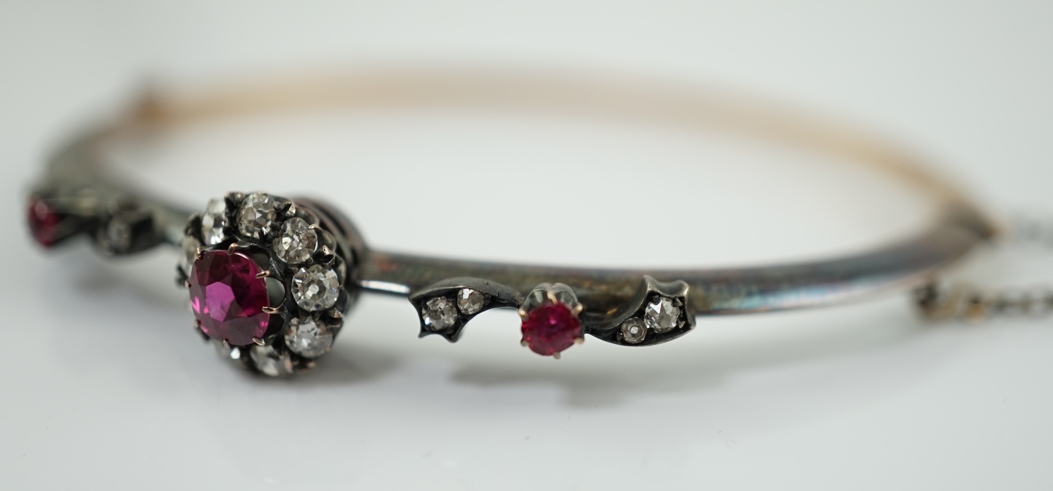 A late Victorian gold and silver, ruby and diamond cluster set hinged bangle